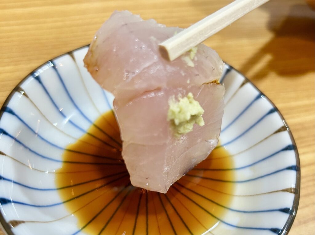 わさびと醤油をつけて箸で持ち上げているカンパチの刺身