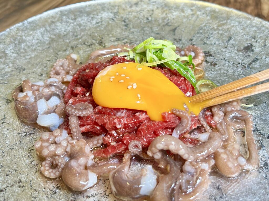 ユッケの卵黄を箸で割っている